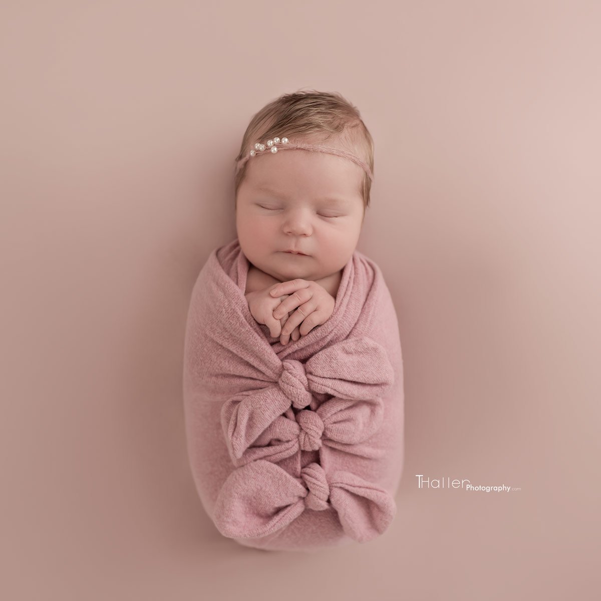 Newborn girl sleeping wrapped in a pink blanket wearing a flower headband