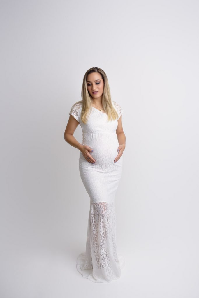 Vancouver Maternity Photographer - Pregnant woman wearing a white lace dress cradling her belly