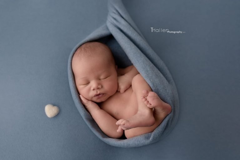 Sleeping newborn in a blue wrap on a blue blanket with a white heart