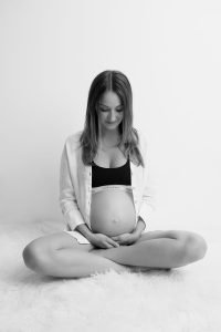 Maternity - Pregnant woman siting with her legs cross crossed and looking at her belly