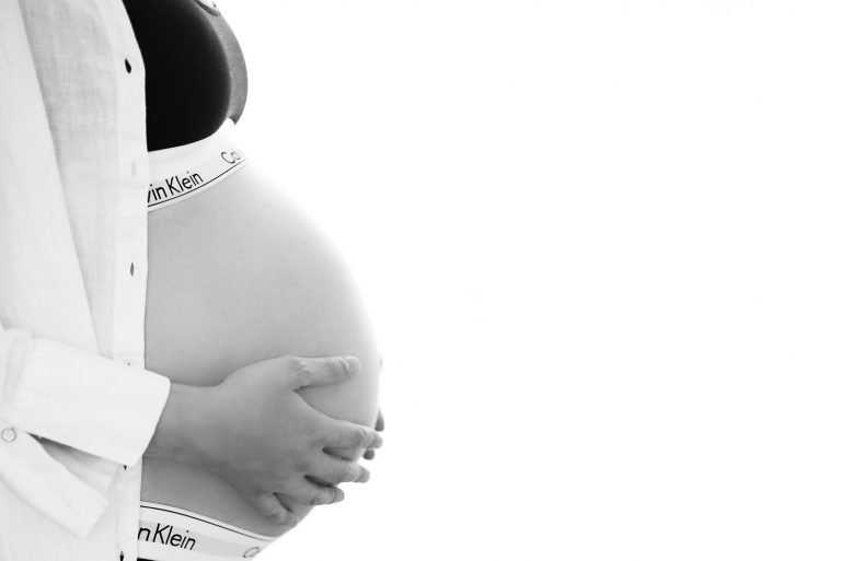 Sideview of a belly of a pregnant woman wearing Calvin Klein underwear and a white shirt