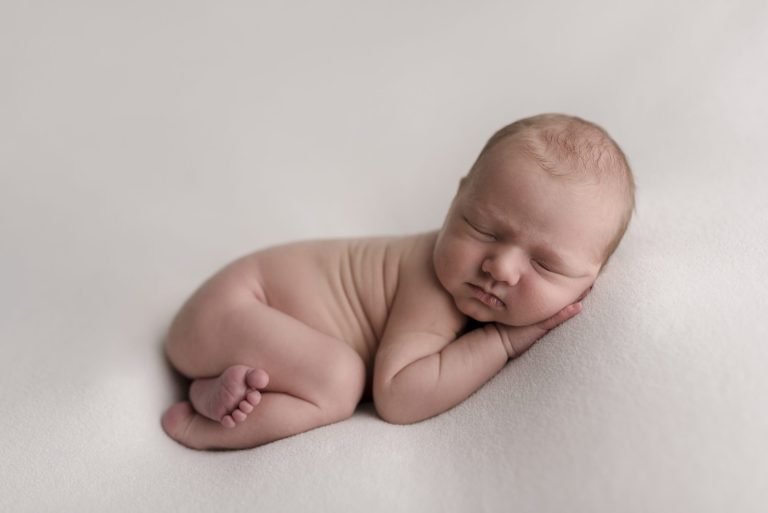 newborn boy sleeping on a neutral blanket with foot peaking out