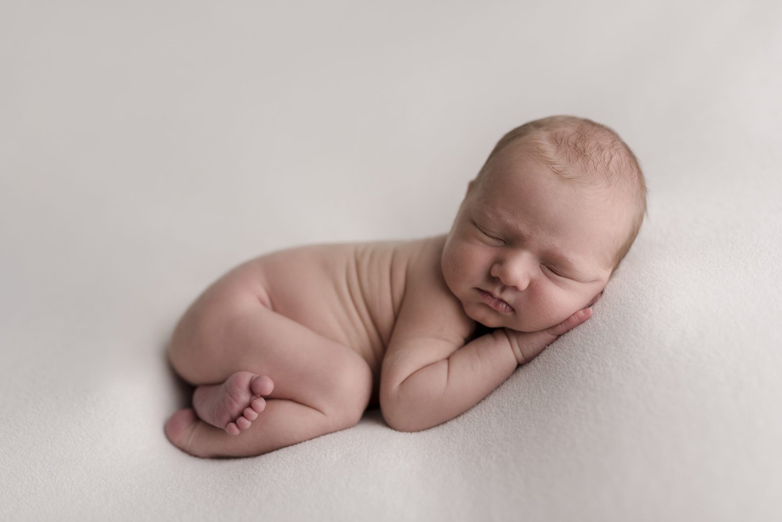 newborn boy sleeping on a neutral blanket with foot peaking out