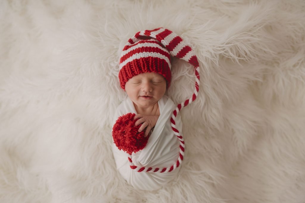 Newborn baby smiling in his sleep wearing a Christmas hat