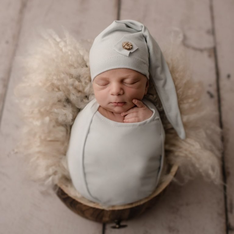 Newborn Baby Boy posed in a bucket with a light blue sleepy hat - shot taken by a professional newborn photographer
