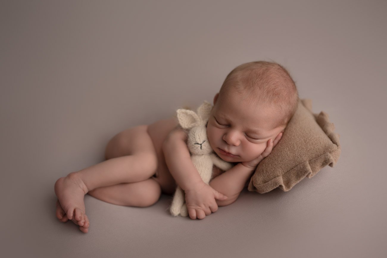 Newborn Baby boy sleeping on a little pillow holding a bunny